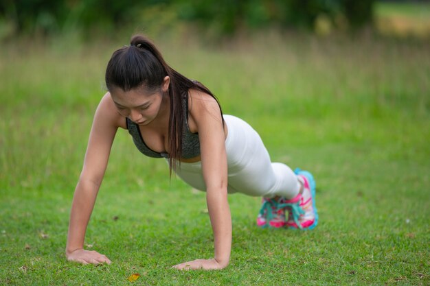 Beautiful woman with long hair exercising on the park lawn.