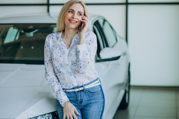 Beautiful woman with phone in car showroom