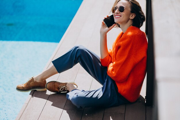 Красивая женщина с телефоном, сидя у бассейна