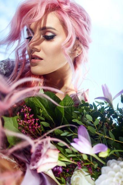 Beautiful woman with pink hair holds large bouquet with greenery and violet flowers