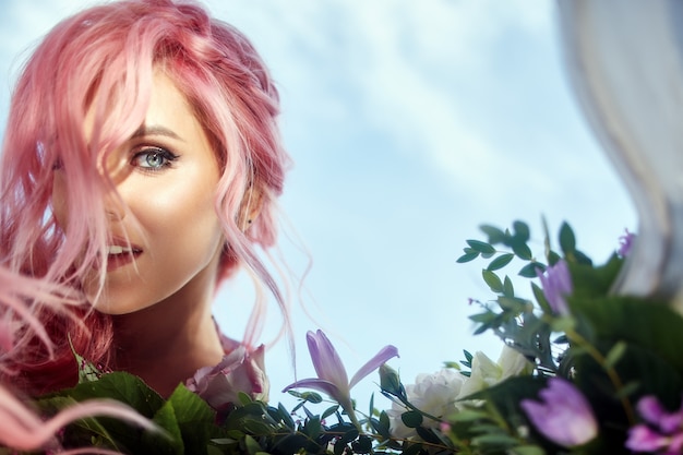 Beautiful woman with pink hair holds large bouquet with greenery and violet flowers