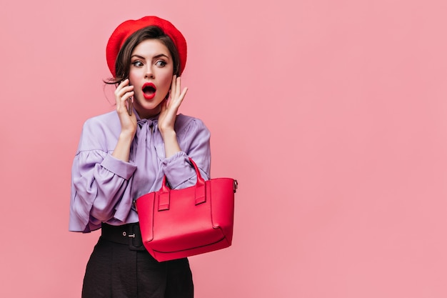 Foto gratuita bella donna con rossetto rosso ha aperto la bocca per la sorpresa. ragazza in berretto e camicetta alla moda in posa con la borsa.