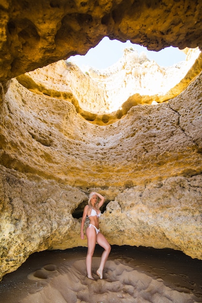 Красивая женщина с сексуальным телом позирует возле скал на пляже