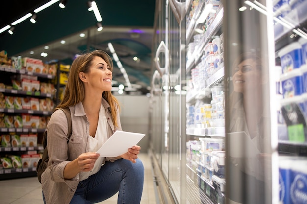 Beautiful woman with shopping list buying food in supermarket