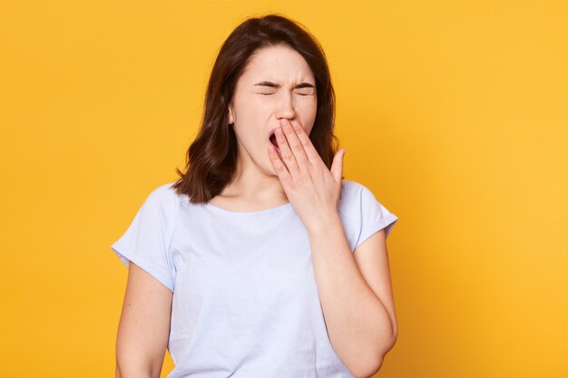 Beautiful woman yawns isolated over yellow