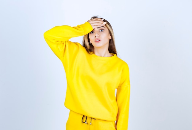 Beautiful woman in yellow sweatsuit having headache over white wall