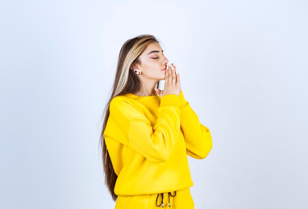 Beautiful woman in yellow sweatsuit standing and posing over white wall