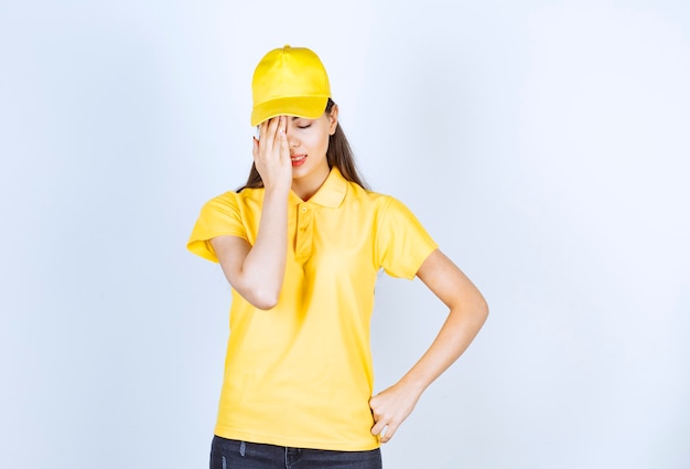 Beautiful woman in yellow t-shirt and cap feeling depressed on white background.