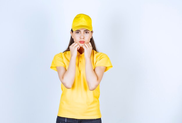 Beautiful woman in yellow t-shirt and cap shocked about something on white background.