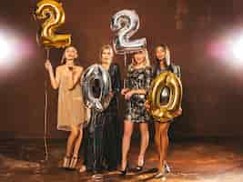 Free photo beautiful women celebrating new year. happy gorgeous girls in stylish sexy party dresses holding gold and silver 2020 balloons, having fun at new year's eve party. holiday celebration.charming models