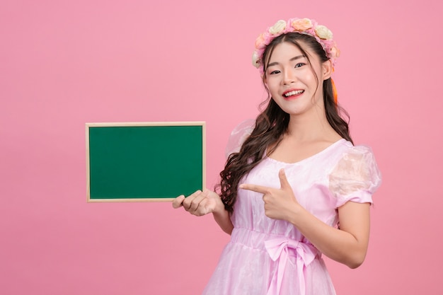 Beautiful women dressed in pink princess dresses hold a green board on a pink .