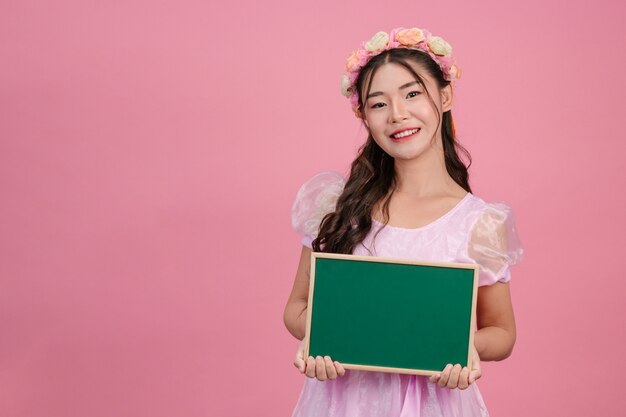 Beautiful women dressed in pink princess dresses hold a green board on a pink .