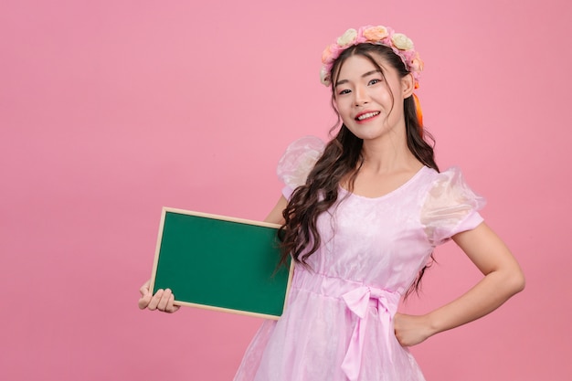 Beautiful women dressed in pink princess dresses hold a green board on a pink .