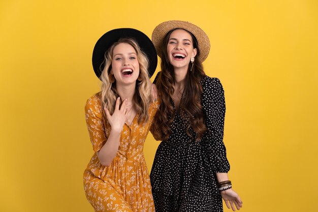 Beautiful women friends together isolated on yellow background in black and yellow dress and hat
