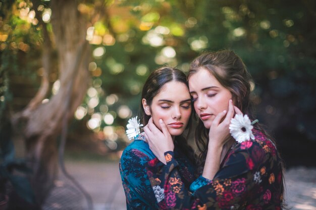 Beautiful women holding flowers and hugging with closed eyes
