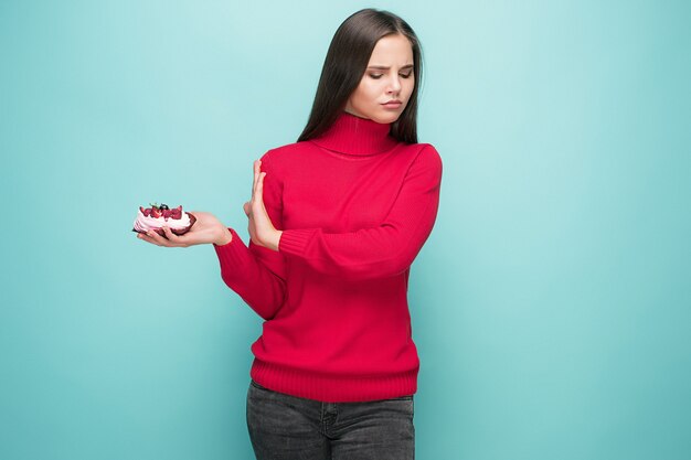 Beautiful women holding small cake. Birthday, holiday, diet. Studio portrait over blue background