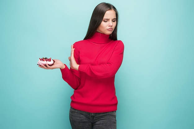 Beautiful women holding small cake. Birthday, holiday, diet. Studio portrait over blue background