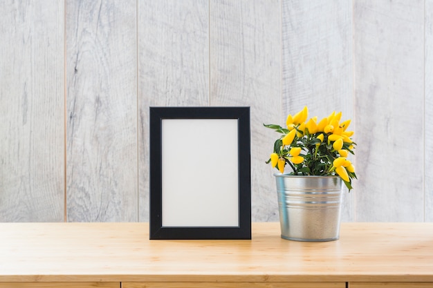 Beautiful yellow hot chili peppers in silver pot and white picture frame on the table