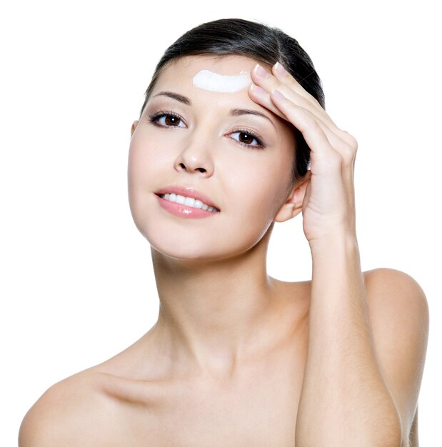 Beautiful young adult smiling female applying cosmetic cream on forehead. 