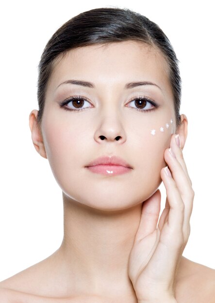 Beautiful young adult woman applying cosmetic cream around the eye