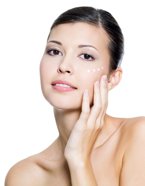 Beautiful young adult woman applying cosmetic cream around the eye