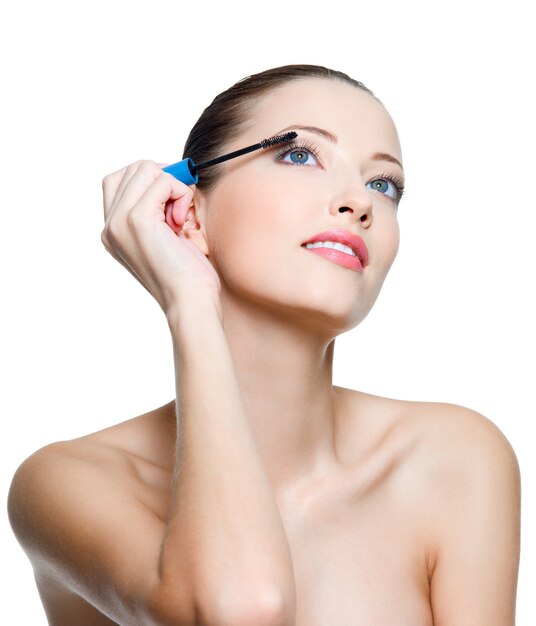 Beautiful young adult woman applying mascara on eyelashes - isolated on white