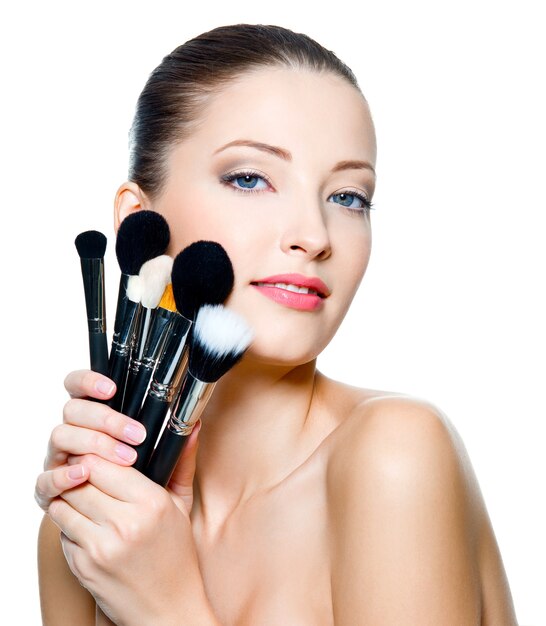 Beautiful young adult woman  holds the make-up brushes near attractive face. Fashion  model posing over white background