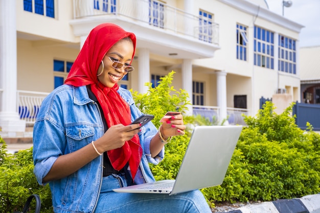 Beautiful young African woman smiling while using her laptop outside