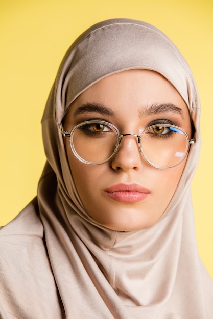copyspace와 노란색 배경에 고립 된 세련 된 hijab에서 아름 다운 젊은 아랍 여성
