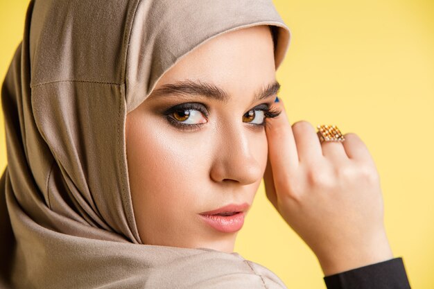 Красивая молодая арабская женщина в стильном хиджабе на желтом фоне с copyspace