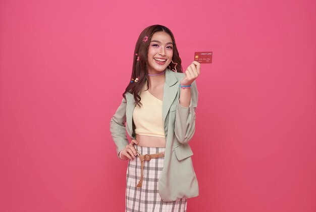 美しい若いアジアのティーンエイジャー女性がオンライン支払いのクレジットカードを提示しているのを笑顔で示しています