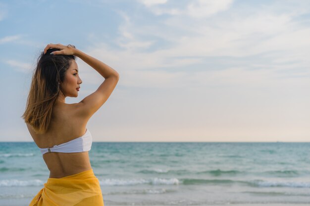 幸せな美しい若いアジア女性は海の近くのビーチの上を歩いてリラックスします。