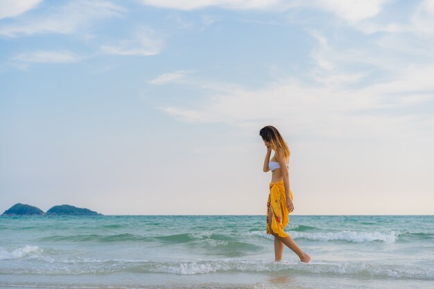 幸せな美しい若いアジア女性は海の近くのビーチの上を歩いてリラックスします。