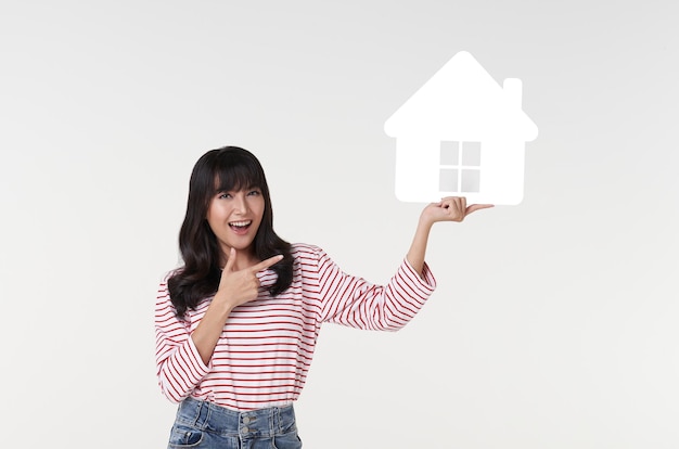 Beautiful young asian woman holding paper house cutout isolated on white background