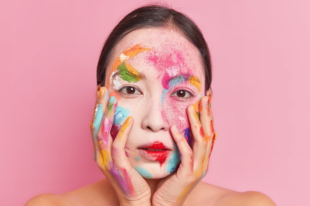 Bella giovane donna asiatica tiene le mani sulle guance ha vernice colorata sul viso