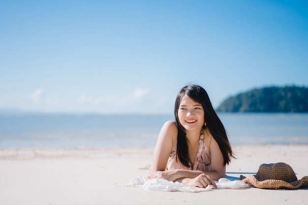 Красивая молодая азиатская женщина лежа на пляже счастливая ослабляет около моря.