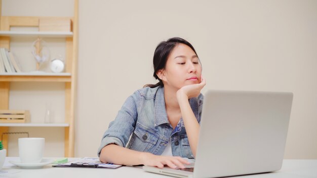 Beautiful young asian woman sleepy exhausted working at office desk at home office, feeling sick and tired.