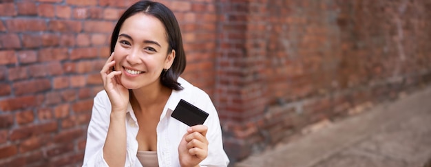 無料写真 ノートパソコンの近くに座って笑顔で請求書を支払うクレジットカードを持つ美しい若いアジアの女性