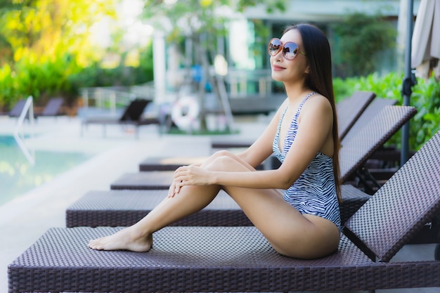 Улыбка красивых молодых азиатских женщин счастливая ослабляет вокруг открытого бассейна в курорте гостиницы