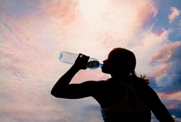 Beautiful young blond girl drinking water in the evening sunset