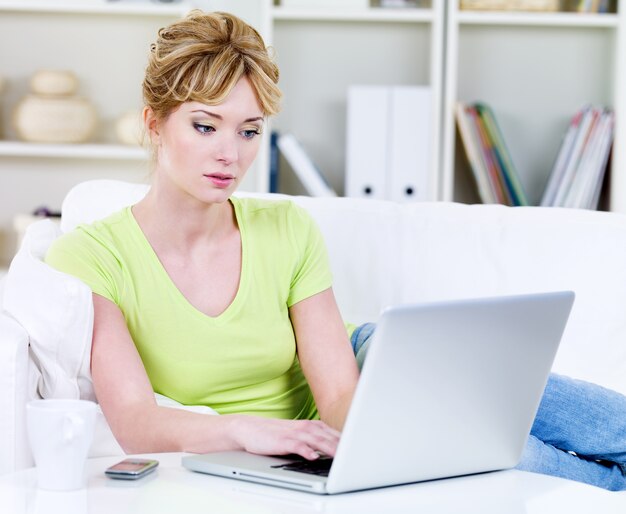 Beautiful young blond woman working with laptop at home - indoors