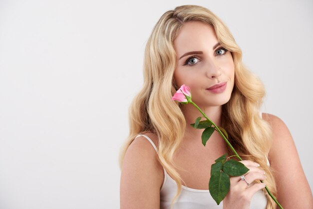 Beautiful young blonde Caucasian woman in camisole top posing with pink rose