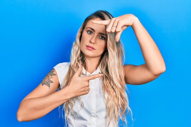 Foto gratuita bella giovane donna bionda che fa il gesto della cornice con le mani rilassate con un'espressione seria sul viso. semplice e naturale guardando la telecamera.