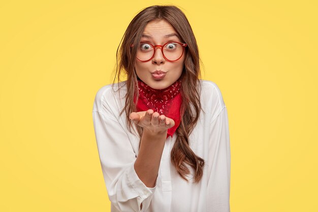 Beautiful young brunette with glasses posing against the yellow wall