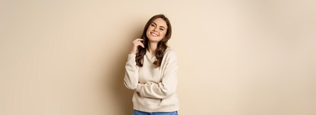 Красивая молодая брюнетка позирует счастливой на бежевом фоне, улыбаясь в камеру в поту