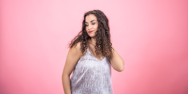 Beautiful young brunette woman with curly hair on a pink background in the studio.