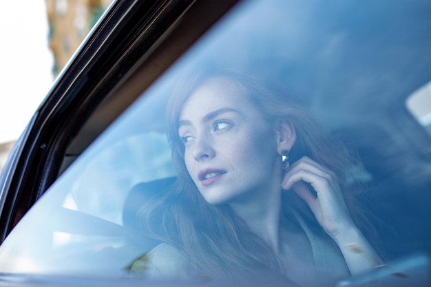 Красивая молодая деловая женщина сидит на заднем сиденье автомобиля и смотрит в окно