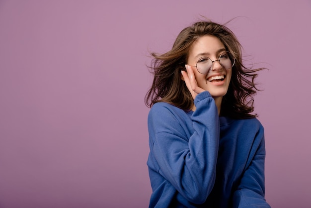 Beautiful young caucasian brunette girl with flying hair wears glasses and hoodie on background with place for text Mood lifestyle concept