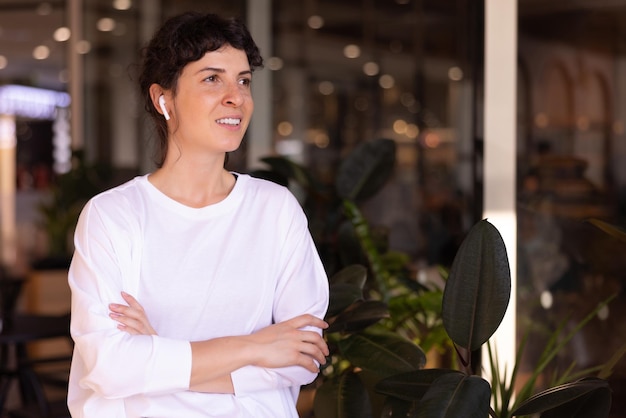 Beautiful young caucasian brunette woman wear white sweater with crossed arms looks away in city indoors