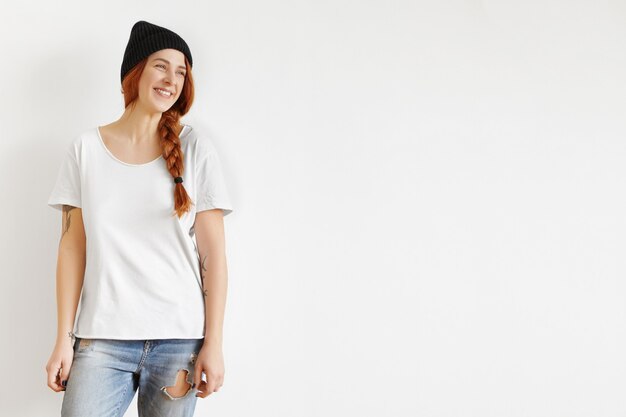 Beautiful young Caucasian female with ginger hair in braid standing isolated against studio wall